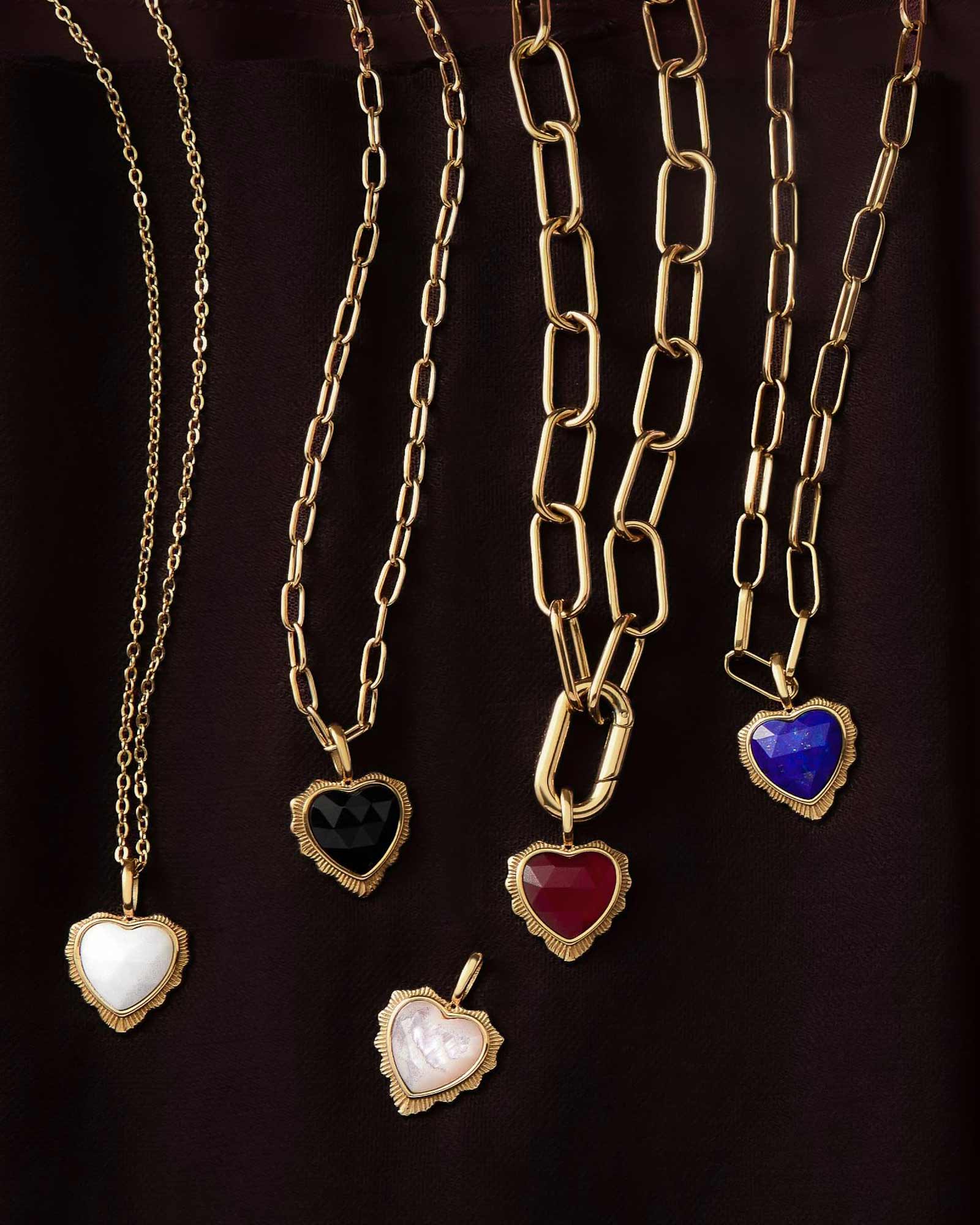 Gold Heart Stone Pendants Range placed on various foundation chains, against a wine red background