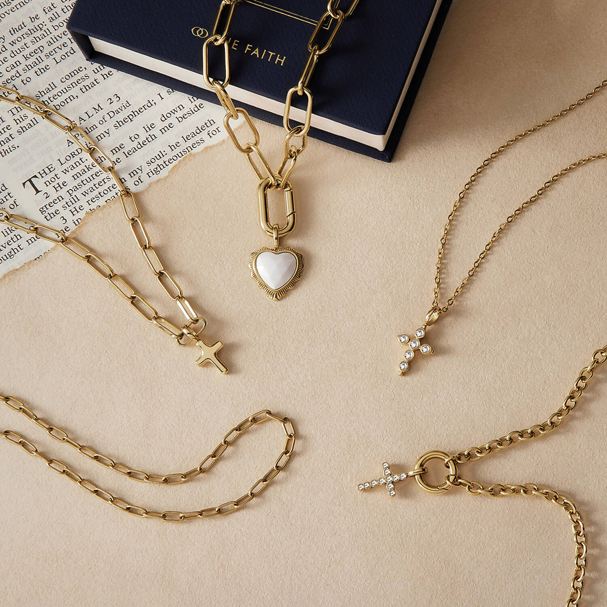 A styled flat-lay image of gold jewelry with The Faith's white onyx heart pendant necklace at the centre.