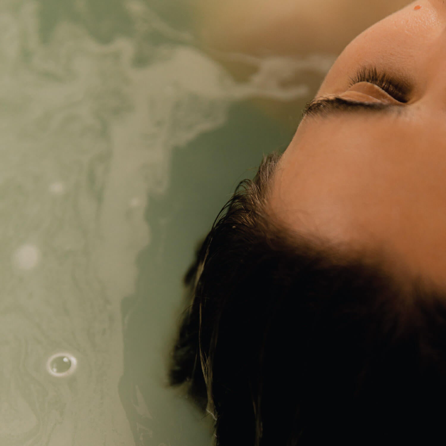 Close-up of a person's face with eyes closed, possibly in a bath or pool.