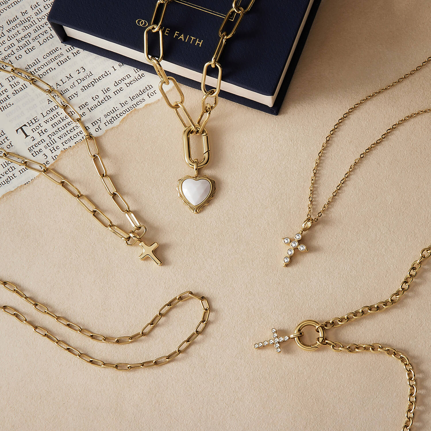A styled flat-lay image of gold jewelry with The Faith's white onyx heart pendant necklace at the centre.
