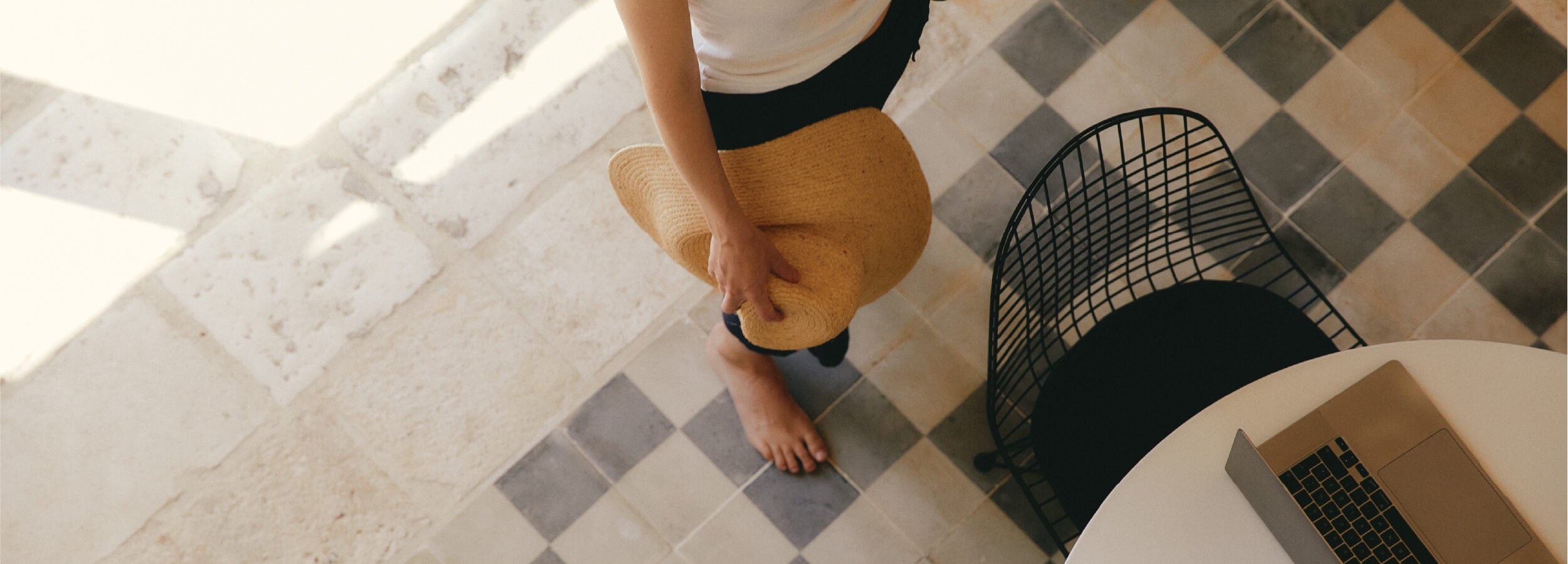 Person standing on a checkered floor with a straw hat and white top.