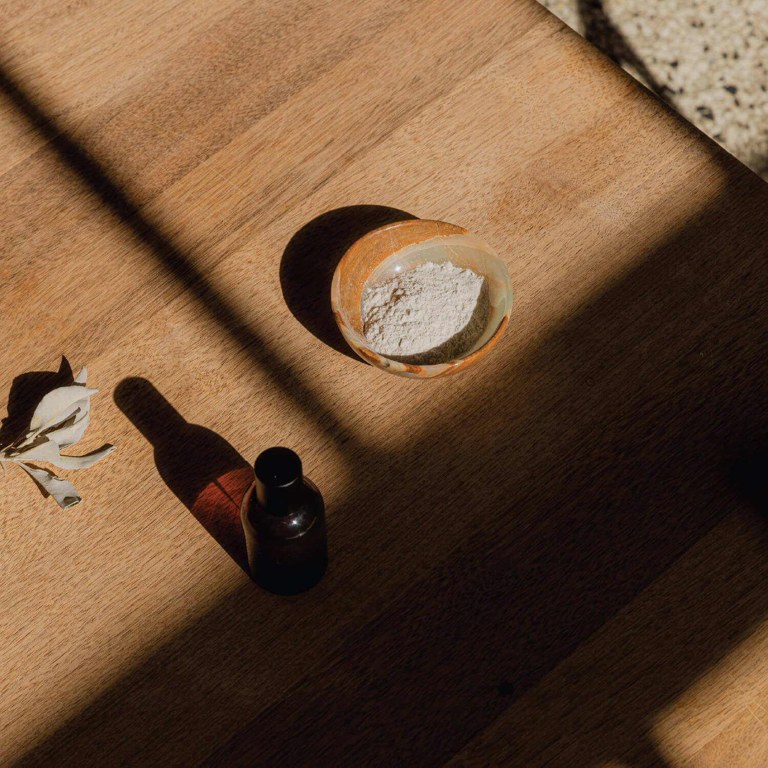 Small glass bowl with powder and bottle on wooden surface