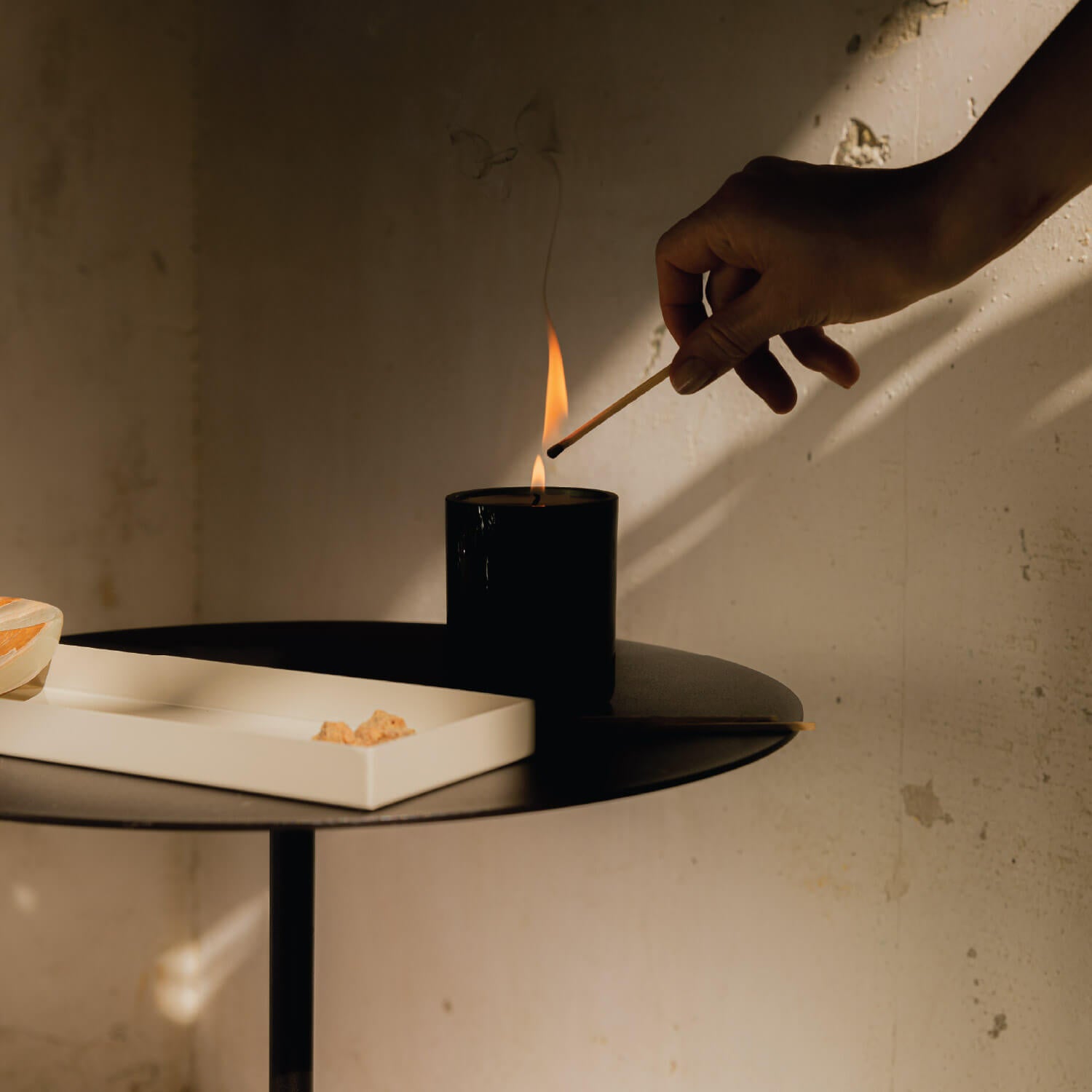Person lighting a black candle on a table with a match.