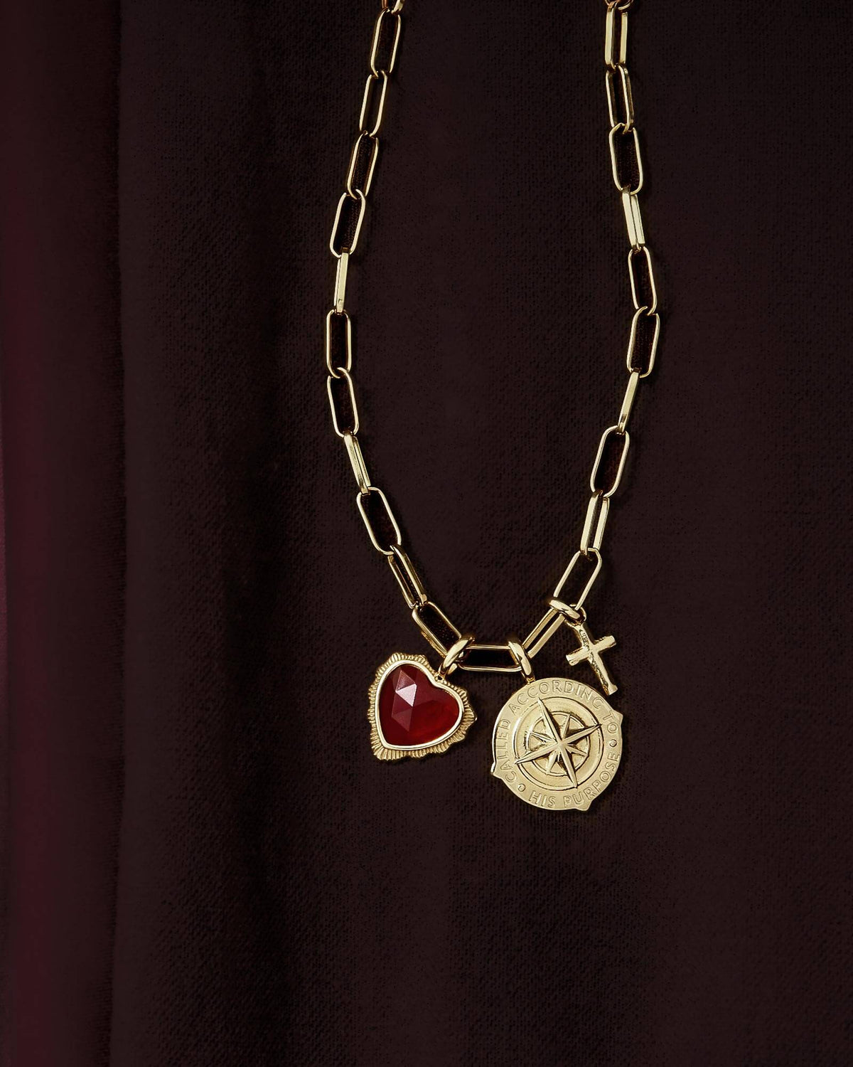 Various Gold Pendants on Gold Foundation Link Chain against a deep red background.