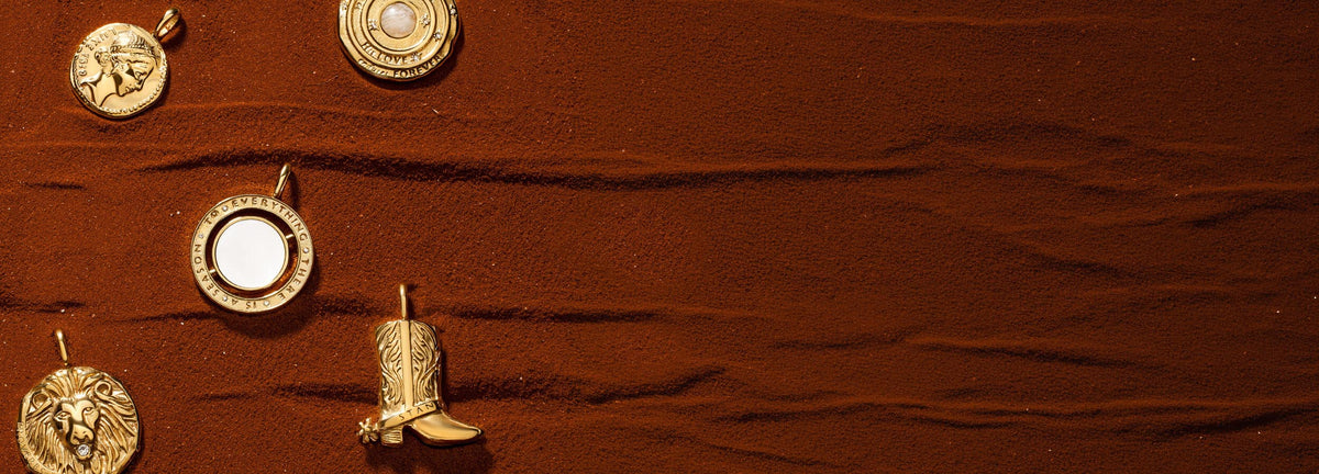 Five gold Christian medallions, including lion, cowboy boot and scripture designs, arranged on sand