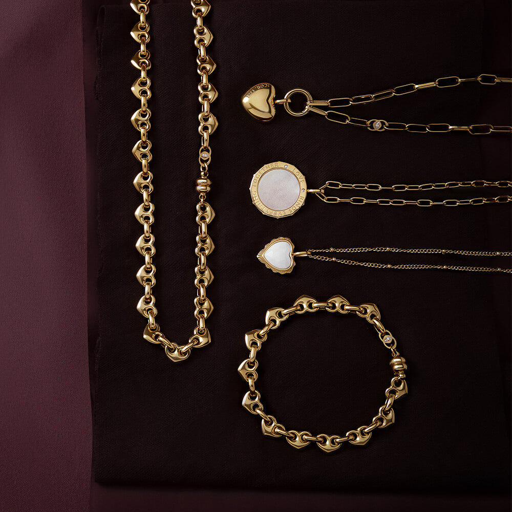 Gold Love scripture necklaces and matching bracelet with heart and mother-of-pearl pendants on burgundy fabric